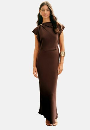 Braunes, ärmelloses Kleid mit drapierter Stoff, einem geknoteten Schulterdetail und schmaler Passform, kombiniert mit einem goldenen Armreif und Blockabsätzen.