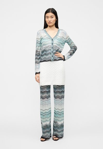 Σετ πλεκτό πολύχρωμο με σχέδιο ζιγκ-ζαγκ, μακριά μανίκια, ζακέτα με λαιμόκοψη σε σχήμα V και παντελόνι φαρδύ σε αποχρώσεις του μπλε, λευκού και μαύρου.