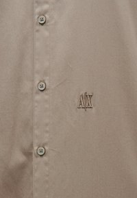 Ανοιχτό καφέ πουκάμισο με κουμπιά, με λεία υφή, που διαθέτει πέντε κουμπιά και κεντημένο λογότυπο "A|X" σε πιο σκούρα απόχρωση.