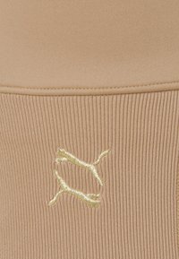 Tissu côtelé beige avec logo Puma doré cousu près d'une couture.