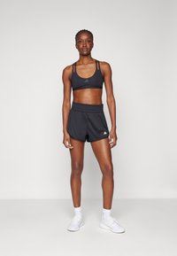 Zwarte sportbeha met dunne bandjes, gecombineerd met zwarte sportshorts met een elastische tailleband. Witte logo-accenten op beide kledingstukken.