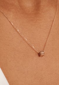 Collier en or rose délicat avec un pendentif en forme de cube arborant un design d'étoile, suspendu sur une fine chaîne contre un fond de teint.
