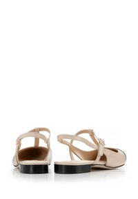 Zapatos de piel beige tipo slingback con punta redondeada, sutil ribete negro y tacón ancho; cuentan con una correa ajustable en el tobillo.