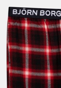 Røde og svarte rutete boxere med en marineblå linning som har teksten "BJÖRN BORG" i hvitt. Materialet ser mykt og teksturert ut.