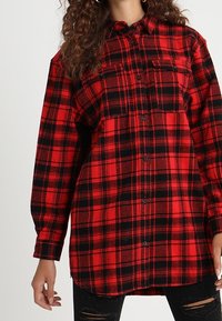 Czerwona i czarna koszula flanelowa w kratę z długimi rękawami, guzikami z przodu, dwoma kieszeniami na piersi i zaokrąglonym dołem. Materiał średniej wagi o miękkiej fakturze.