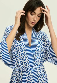 Niebieska i biała, wzorzysta szata z lekkiego materiału, z geometrycznymi wzorami i paskami, z głębokim dekoltem w serek i szerokimi rękawami.