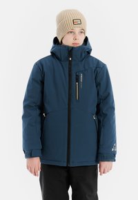 Blaues Jackett mit Reißverschluss vorne, Kapuze und Reißverschlusstaschen. Mit gerippten Bündchen und einem Logo-Patch auf der linken Brust. Kombiniert mit einer beigen Mütze.