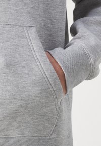 Grauer Sweatshirt mit Kängurutasche, gerippten Bündchen und weichem Baumwollmix. Nahaufnahme zeigt die Textur und die Nahtdetails.