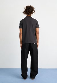 Polo shirt noir à manches courtes en coton épais, associé à un pantalon noir ample. Coutures visibles et design de col classique.