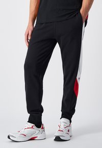 Black athletic pants with red and white side panels. Made of soft fabric, featuring a tapered design with elastic cuffs and side pockets.