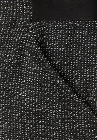 Musta kangas, jossa on tekstuurillisia valkoisia pilkkuja ja poikkijuovittainen kuvio. Yläosa on sileä ja siinä on yksivärinen musta reunus.