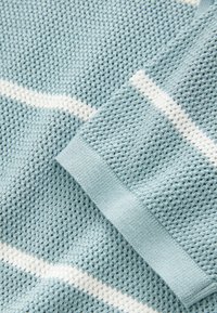 Primer plano de tela de punto azul claro con textura de panal y rayas horizontales blancas. Incluye un puño doblado con borde acanalado.