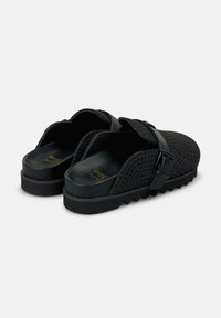 Zoccoli neri con apertura sul retro realizzati in materiale testurizzato, dotati di un robusto cinturino con fibbia e una suola spessa e scanalata. L'interno presenta una finitura liscia.