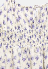 Tessuto leggero di colore crema con un motivo floreale in viola. Presenta dettagli smock e una chiusura con cravatta sul retro. Texture morbida.