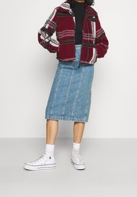 Veste polaire rayée rouge et blanche avec col, associée à une jupe midi en jean avec coutures verticales et des baskets blanches.