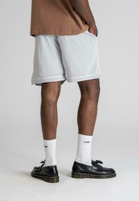 Light gray mesh shorts with contrasting white trim, paired with black lace-up shoes and white socks. Focus on breathable fabric and casual fit.
