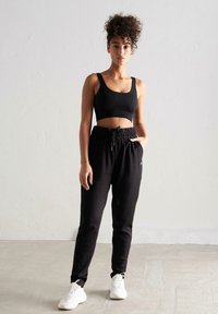 Sort ribbet crop top parret med sorte joggerbukser med elastisk talje og sidelommer, suppleret af hvide sneakers.