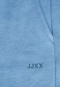 Lichtblauwe gebreide stof met een zakje en donkerblauwe letters "JJXX" gedrukt vlakbij de opening van het zakje.