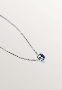 Collar de cadena de plata que presenta una gema azul ovalada central, engastada en un delicado diseño de garras con pequeñas piedras de acento.