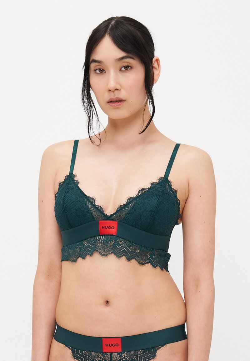 Teal blonde bralette med justerbare stropper, bølgede kanter og en rød merkeetikett i midten. Kombinert med matchende teal blonde truser.