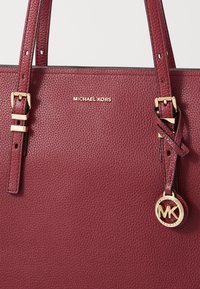 Borsa tote bordeaux Michael Kors in pelle testurizzata, con hardware color oro e un pendente con il logo, dotata di doppi manici per la spalla.