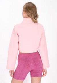 Rosa kort sweatshirt med långa ärmar och hög krage, matchad med texturerade rosa shorts i en figurnära design.
