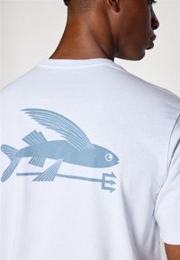 Camiseta de algodón blanca con un gráfico azul de un pez con alas y un tridente. El diseño está ubicado en la parte posterior de la camiseta.