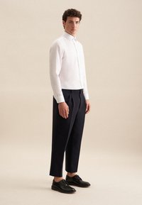 Biała koszula z długim rękawem, w zestawieniu z ciemnymi spodniami i czarnymi sznurowanymi butami. Prosty wzór, dopasowany krój, gładka tekstura.