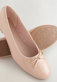 Helle rosa Lack-Ballerinas mit runder Spitze, die ein kleines Schleifendetail und strukturierte braune Sohlen aufweisen. Glattes Material und schlichtes Design.