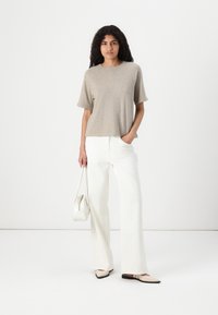 Beige short-sleeve top paired with white wide-leg pants. The model holds a small white handbag and wears light-colored flats.