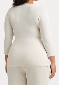 Långärmad, ljusbeige topp i stretchigt material, med rund halsringning och sidslitsar i nederkanten för ökad rörlighet.