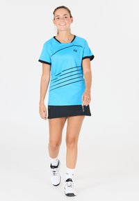 Blå idrottströja med svarta accenter och horisontella ränder, i kombination med en svart kjol och vita sneakers, som visar en sportig design.