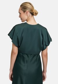 Grøn satindragt med korte, flagrende ærmer, en rund halsudskæring og en tætsiddende talje. Glat tekstur og subtil glans er synlig.