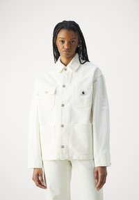 Veste en denim blanc avec col, boutons sur le devant et deux poches poitrine. Caractéristiques de coutures visibles et d'un patch logo sur la poche gauche.