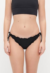 Crni bikini donji dio s naboranim rubom, podesivim bočnim vezicama i glatkom teksturom. Tkanina je meka i u solidnoj boji.