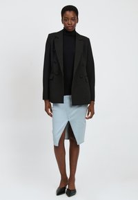 Blazer doppiopetto nero con bottoni rotondi, abbinato a una gonna di jeans azzurro chiaro con uno spacco frontale. Tacchi a punta neri.