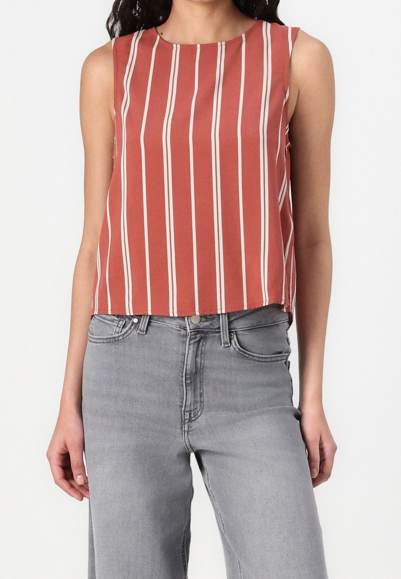 Haut sans manches rouge rouille avec des rayures blanches verticales porté avec un jean taille haute gris clair sur une personne debout.