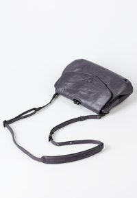 Borsa a tracolla grigia in pelle con patta arrotondata, tracolla regolabile e chiusura a scatto. Presenta una texture morbida e un design minimalista.