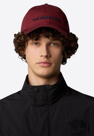 Cappellino da baseball color marsala con logo ricamato "THE NORTH FACE" in blu scuro. Materiale in cotone con visiera curva e cinturino regolabile.