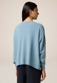 Vaaleansininen ylisuuri neulepaita, jossa on pyöreä pääntie, pitkät hihat ja ribbaushelma. Pehmeä rakenne ja rento istuvuus, yhdistetty tummiin housuihin.