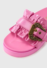 Roza natikača s naboranim satenskim remenom i ukrasnom kopčom u zlatnoj boji. Teksturirana potplata i glatki gornji dio, s upečatljivom, svijetlom bojom.