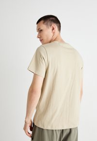 T-shirt in cotone beige con scollatura rotonda, maniche corte e vestibilità rilassata. Tessuto morbido, senza motivi, design minimalista.