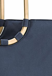 Sac fourre-tout bleu marine en tissu texturé, avec une poignée circulaire dorée et des accents en tissu aux points d'attache.