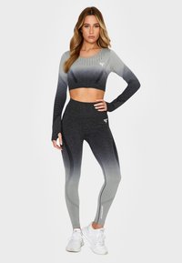 Grå ombre træningssæt bestående af en langærmet crop top med ribbede detaljer og højtaljede leggings med elegante linjer. Hvid logo-detalje.