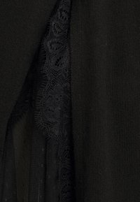 Lähikuva mustasta kangast, mis näitab kudumise tekstuuri, kõrval keerulise lilleline pitsdetail läbipaistval võrgumaterjalil.