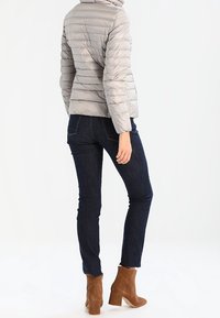 Szara kurtka puchowa z poziomym przeszyciem, zestawiona z ciemnogranatowymi dżinsami i brązowymi botkami na obcasie, widok od tyłu.