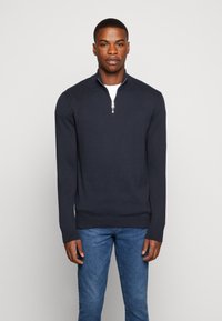 Pullover navy albastru cu fermoar, realizat dintr-o țesătură netedă. Dispune de un guler scurt și de manșete și tiv cu elastic. Asortat cu blugi albastre.
