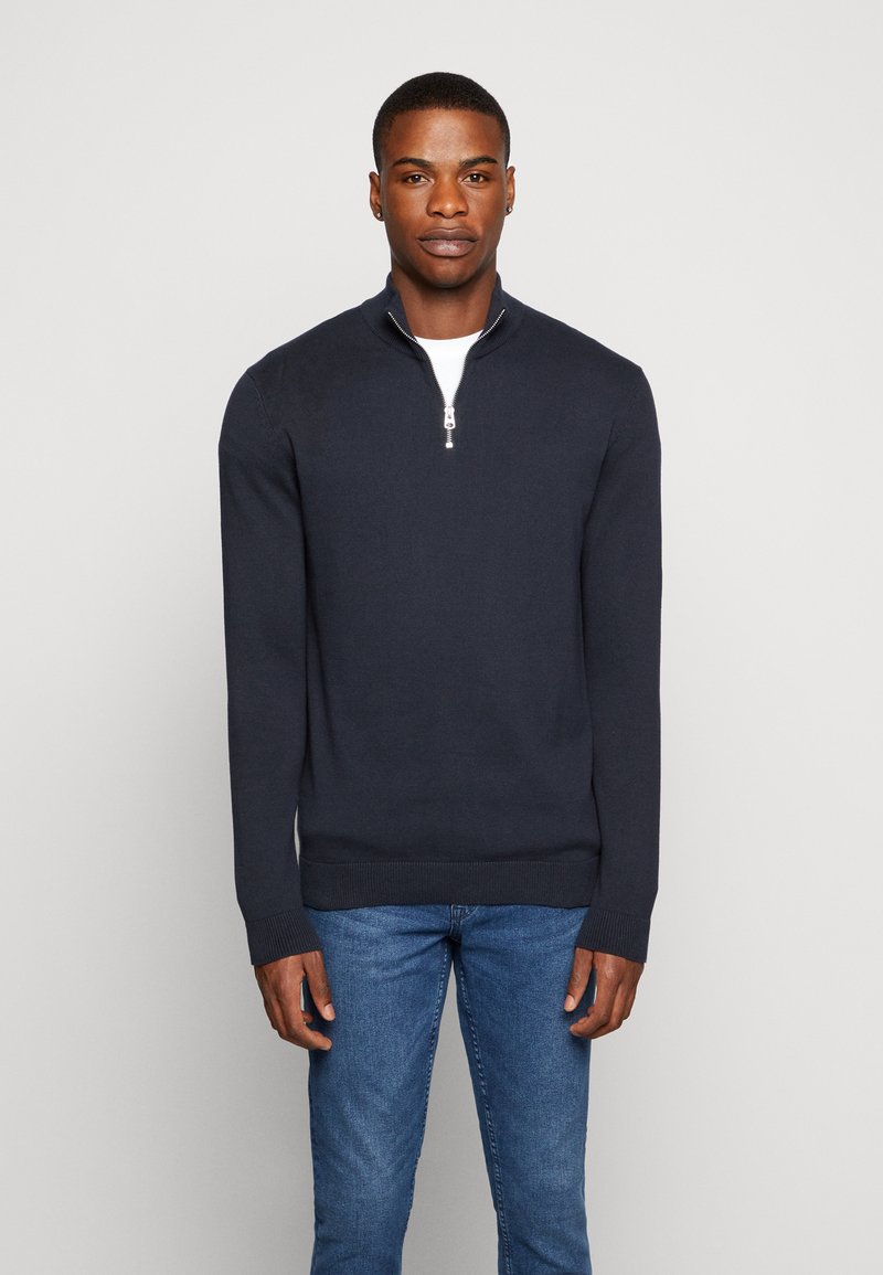 Pullover navy albastru cu fermoar, realizat dintr-o țesătură netedă. Dispune de un guler scurt și de manșete și tiv cu elastic. Asortat cu blugi albastre.