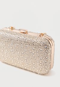 Rhinestone rotāta somiņa ar metālisku rāmi, kas satur zelta toņa sprādzi un faktūru. Kompakta taisnstūra forma.