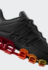 Crna sportska cipela s teksturiranim gornjim dijelom, detaljima u obliku tri pruge i višenamjenskim potplatom s gradijentom boja od narančaste do crvene.